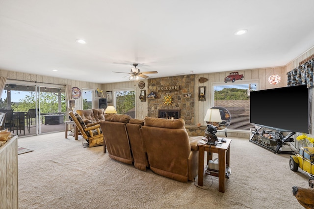 carpeted living room with wood walls, a healthy amount of sunlight, a ceiling fan, and a stone fireplace