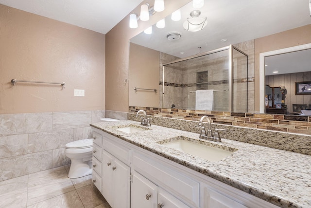 full bathroom with tile walls, a sink, a shower stall, and double vanity