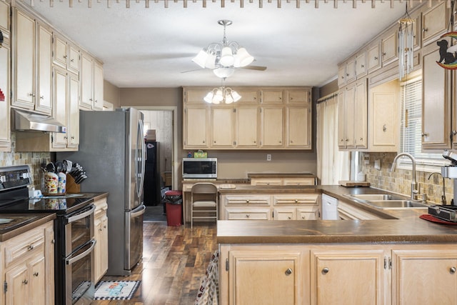 kitchen with a sink, a chandelier, under cabinet range hood, dark countertops, and appliances with stainless steel finishes