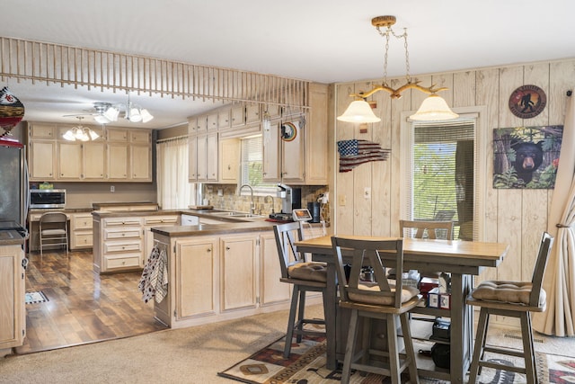 kitchen featuring stainless steel microwave, a sink, wood walls, light brown cabinets, and decorative light fixtures