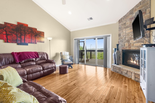 living area with wood finished floors, ornamental molding, a stone fireplace, visible vents, and lofted ceiling