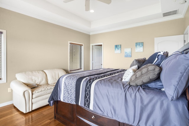 bedroom featuring a raised ceiling, visible vents, baseboards, ornamental molding, and wood finished floors