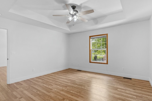 empty room with ceiling fan, visible vents, baseboards, light wood finished floors, and a tray ceiling