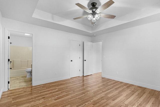 unfurnished bedroom with baseboards, ensuite bathroom, ceiling fan, a raised ceiling, and light wood finished floors