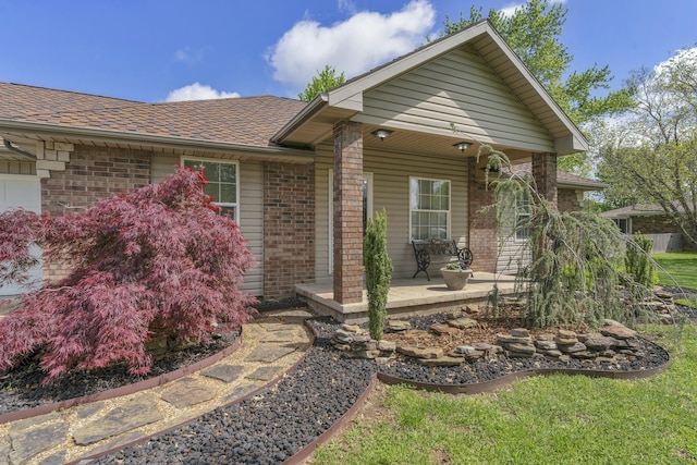 view of front of house featuring roof with shingles, covered porch, and brick siding