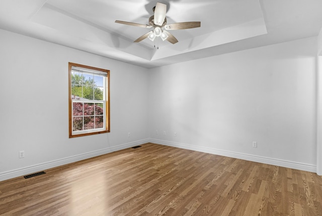 spare room featuring visible vents, wood finished floors, baseboards, a tray ceiling, and a ceiling fan
