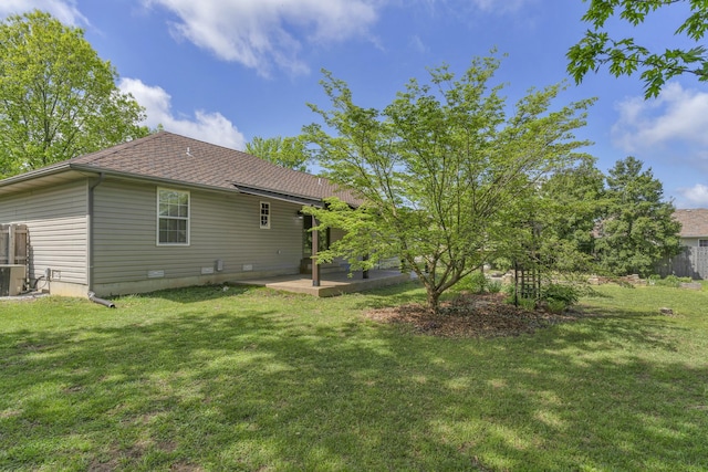 rear view of property featuring roof with shingles, central AC unit, a yard, and a patio area