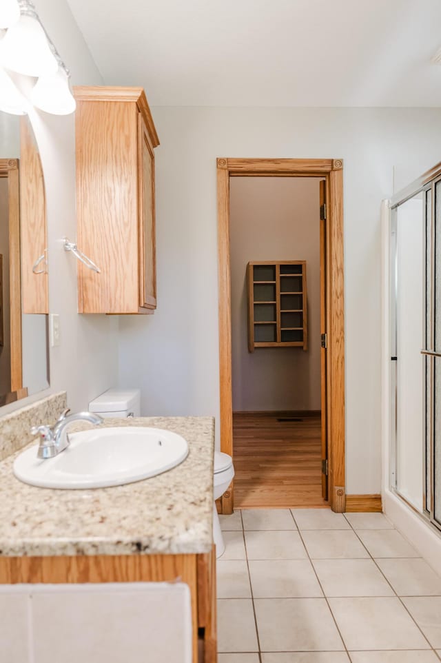 bathroom featuring vanity, toilet, tile patterned floors, baseboards, and a shower stall