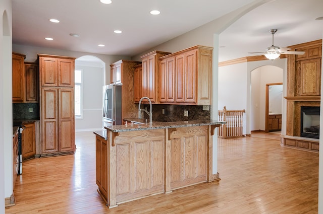 kitchen featuring freestanding refrigerator, a sink, arched walkways, and a peninsula