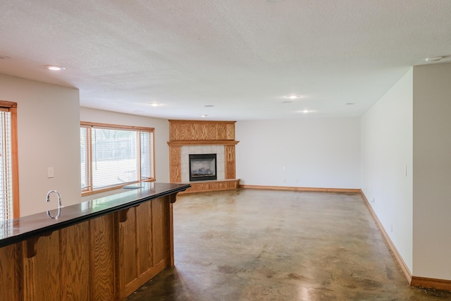 unfurnished living room with finished concrete flooring, baseboards, recessed lighting, a textured ceiling, and a tile fireplace