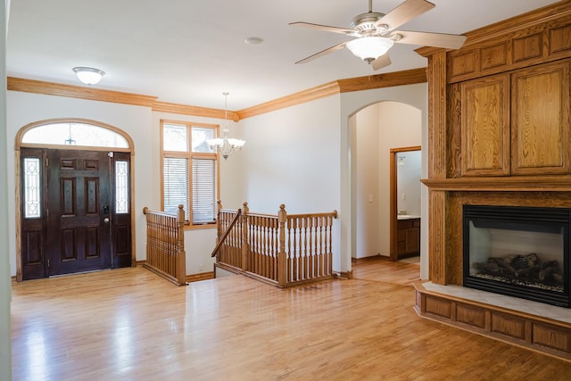 entrance foyer with crown molding, arched walkways, light wood-style floors, and a fireplace