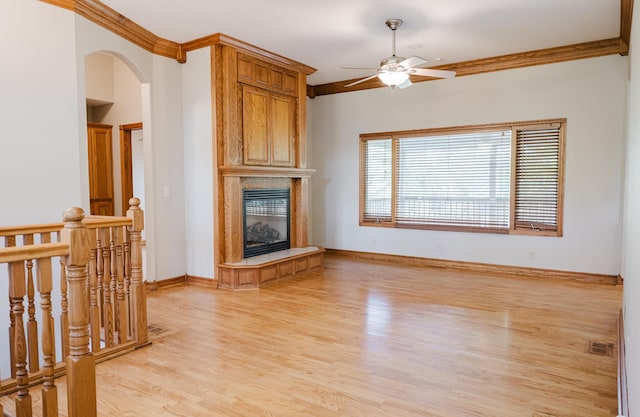unfurnished living room featuring ceiling fan, a fireplace, light wood-style floors, visible vents, and ornamental molding