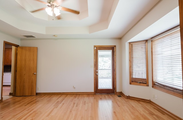 empty room with ceiling fan, baseboards, light wood-type flooring, a tray ceiling, and visible vents