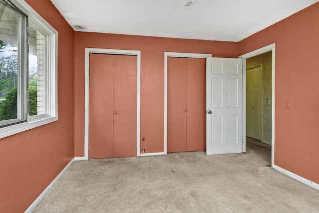 unfurnished bedroom with two closets, baseboards, and light colored carpet