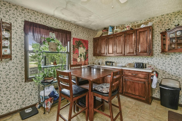interior space featuring baseboards, light countertops, a textured ceiling, and wallpapered walls