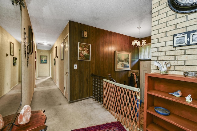 hallway with wood walls, a textured ceiling, and a notable chandelier