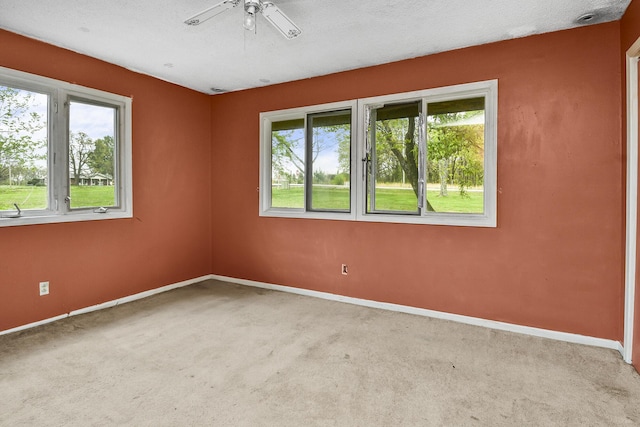 carpeted empty room featuring a ceiling fan, baseboards, and a wealth of natural light