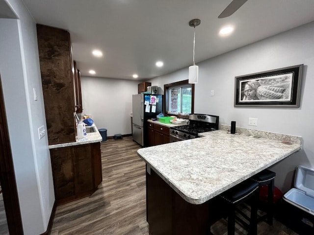 kitchen featuring light countertops, stainless steel appliances, a peninsula, a kitchen bar, and dark wood-style floors