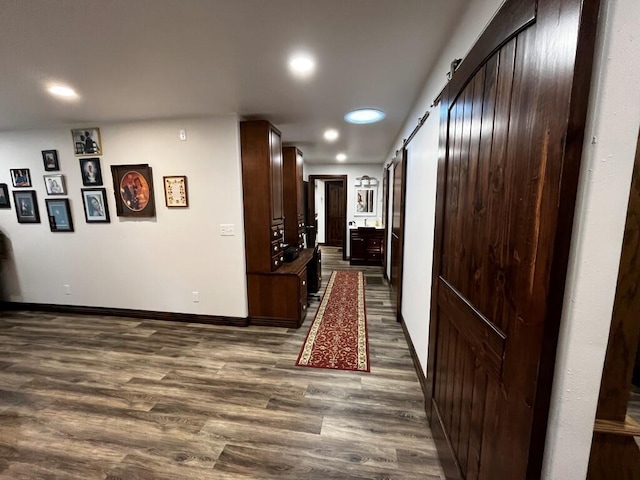 hall with dark wood-type flooring, recessed lighting, baseboards, and a barn door