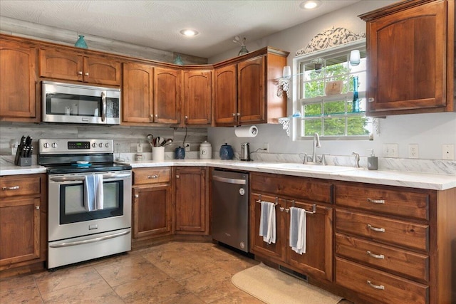 kitchen featuring backsplash, appliances with stainless steel finishes, brown cabinets, a sink, and light countertops