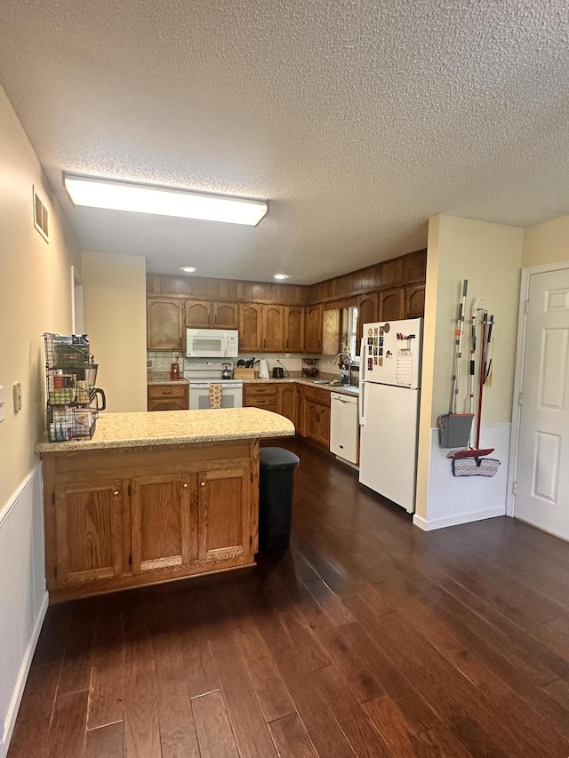 kitchen featuring visible vents, a peninsula, white appliances, light countertops, and a sink