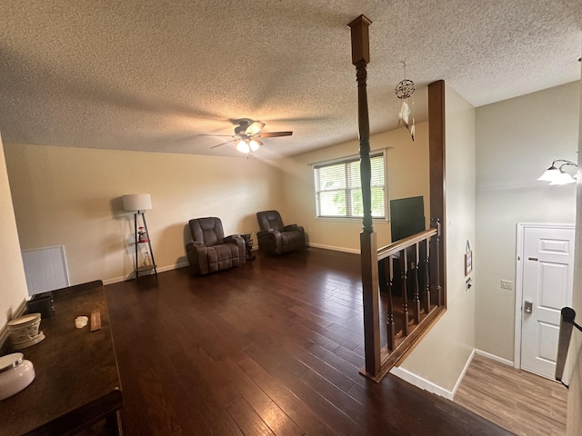 living area with a textured ceiling, ceiling fan, baseboards, and dark wood-type flooring