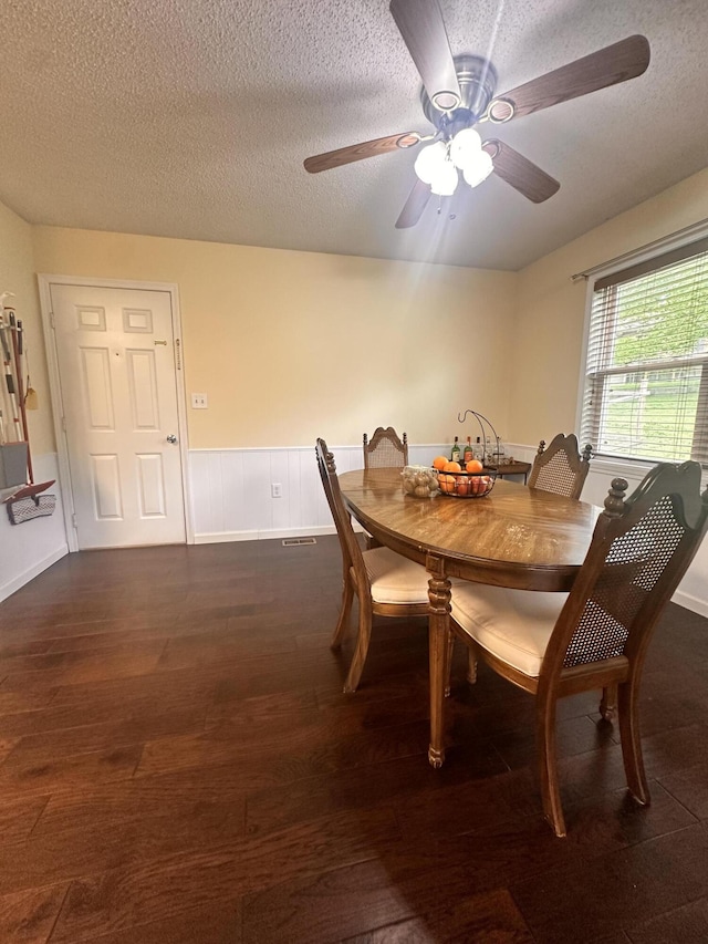 dining space featuring a ceiling fan, a textured ceiling, dark wood finished floors, and wainscoting