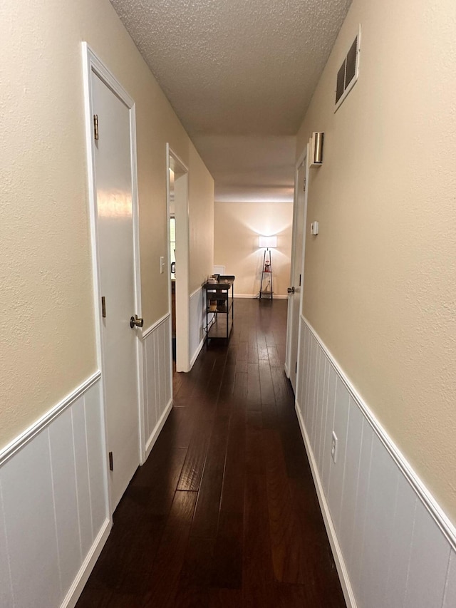 hall featuring a textured ceiling, a wainscoted wall, hardwood / wood-style floors, and visible vents