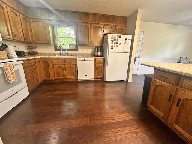 kitchen with brown cabinets, a sink, white appliances, a textured ceiling, and dark wood-type flooring
