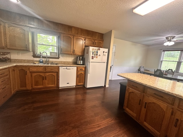 kitchen featuring white appliances, a textured ceiling, brown cabinetry, and a sink