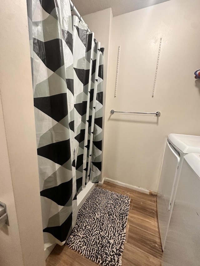 full bathroom with washing machine and clothes dryer, a shower with curtain, and wood finished floors