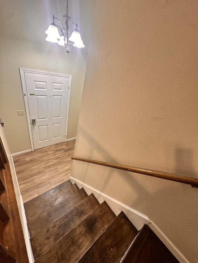 stairs featuring baseboards, an inviting chandelier, and wood finished floors