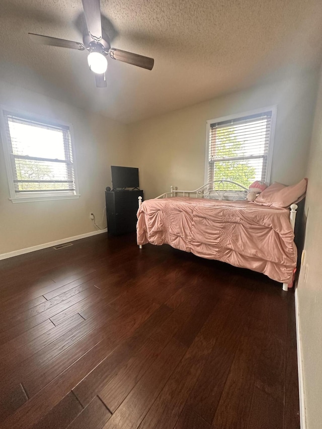 bedroom with a ceiling fan, a textured ceiling, multiple windows, and dark wood-type flooring