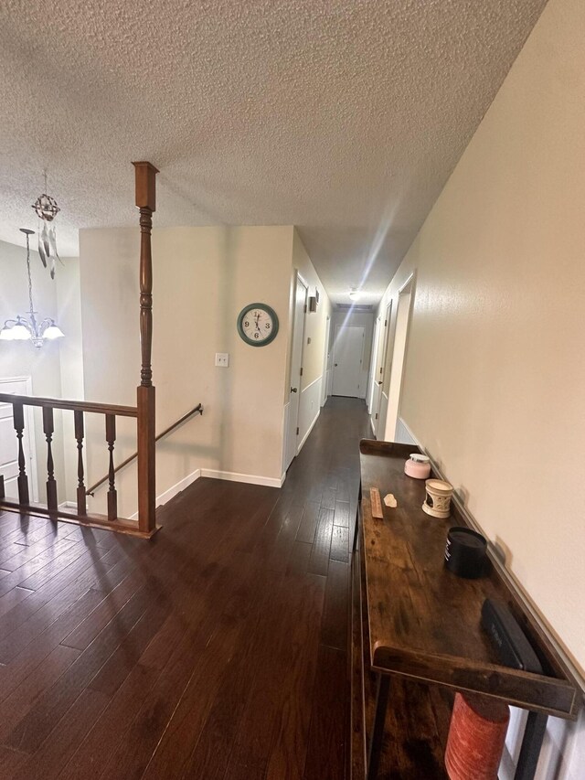 corridor with baseboards, dark wood-style floors, a textured ceiling, a chandelier, and an upstairs landing