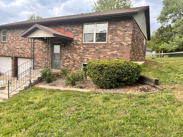 split foyer home featuring brick siding, a front lawn, an attached garage, and fence