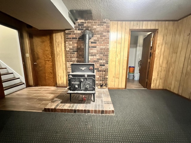 carpeted living area featuring wooden walls, stairway, and a wood stove