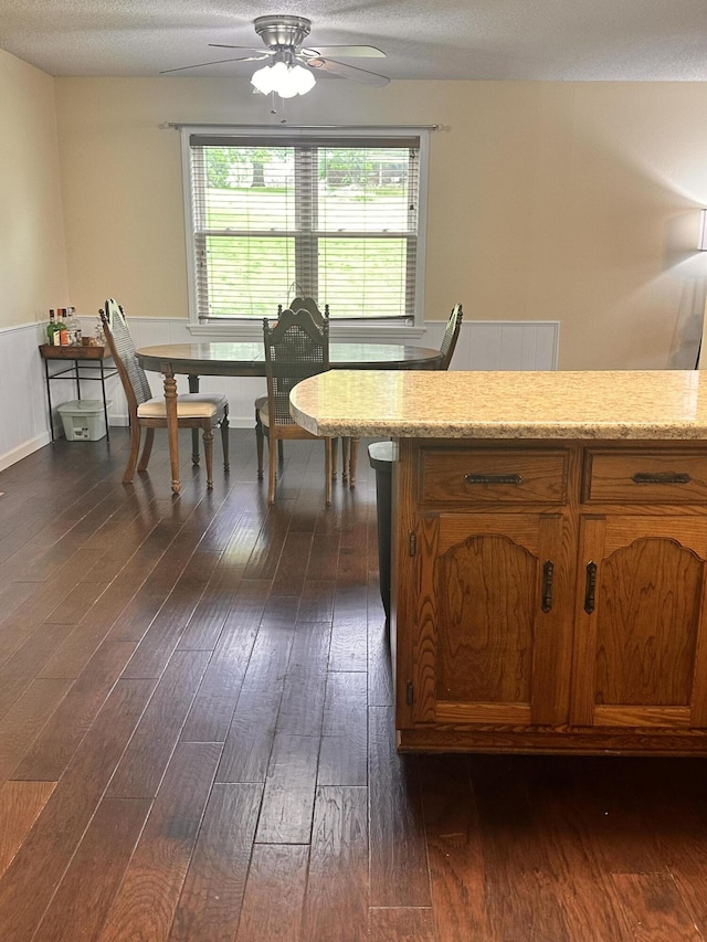 kitchen with brown cabinetry, a ceiling fan, a textured ceiling, light stone counters, and dark wood-type flooring