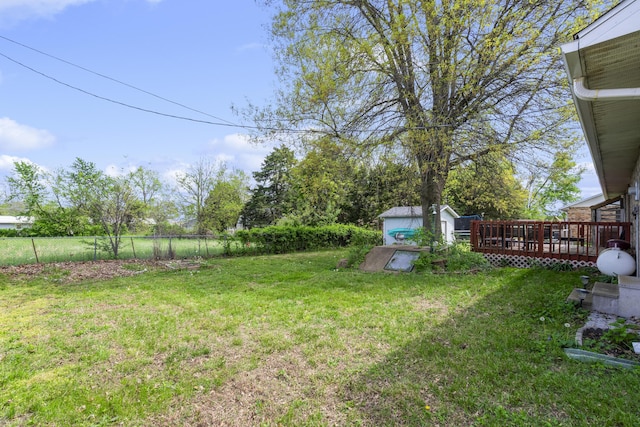 view of yard with fence, a wooden deck, and a storage shed