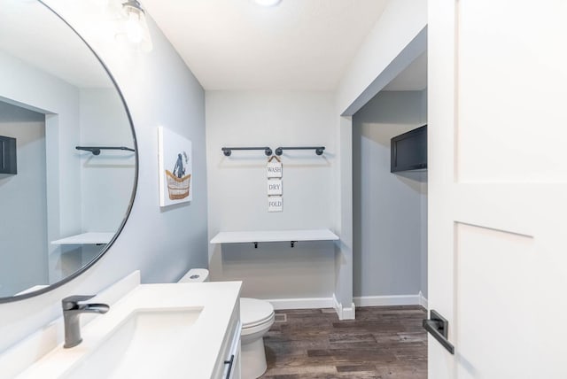 half bath featuring vanity, baseboards, wood finished floors, and toilet