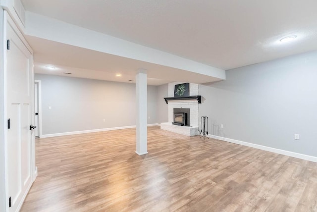 finished basement with light wood-style floors, baseboards, and a brick fireplace