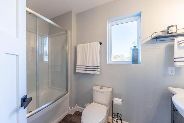 bathroom featuring vanity, toilet, enclosed tub / shower combo, baseboards, and wood finished floors