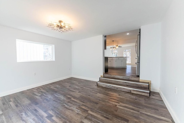 spare room featuring baseboards, dark wood finished floors, and a notable chandelier