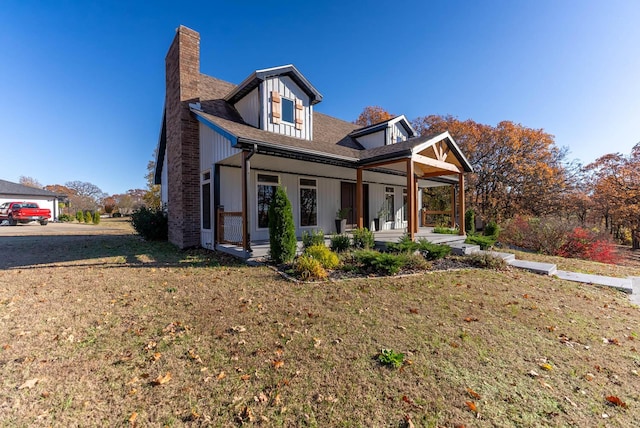view of front of property with covered porch, a chimney, and a front yard