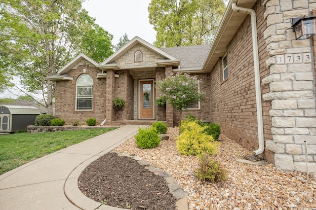 view of front of home with brick siding, an outdoor structure, a shed, a front lawn, and a shingled roof