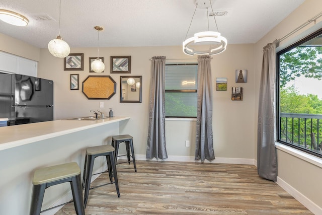 kitchen with pendant lighting, white cabinets, freestanding refrigerator, light wood finished floors, and a breakfast bar