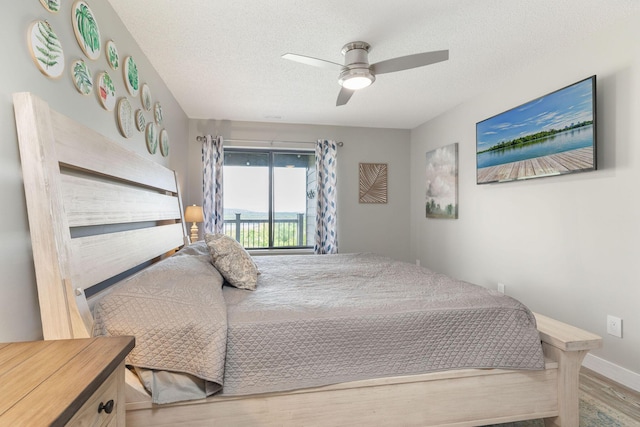 bedroom featuring ceiling fan, a textured ceiling, access to exterior, wood finished floors, and baseboards
