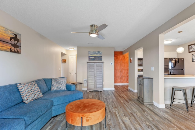 living room featuring baseboards, a textured ceiling, ceiling fan, and wood finished floors