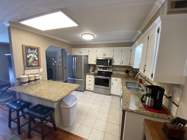 kitchen featuring appliances with stainless steel finishes, a sink, a peninsula, white cabinetry, and ornamental molding