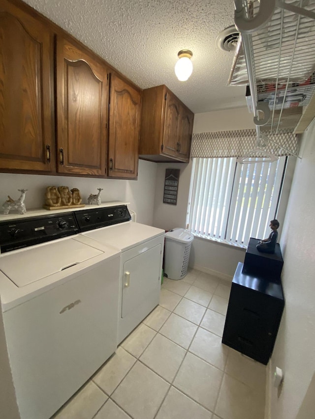 laundry area featuring a textured ceiling, cabinet space, light tile patterned floors, baseboards, and washer and dryer