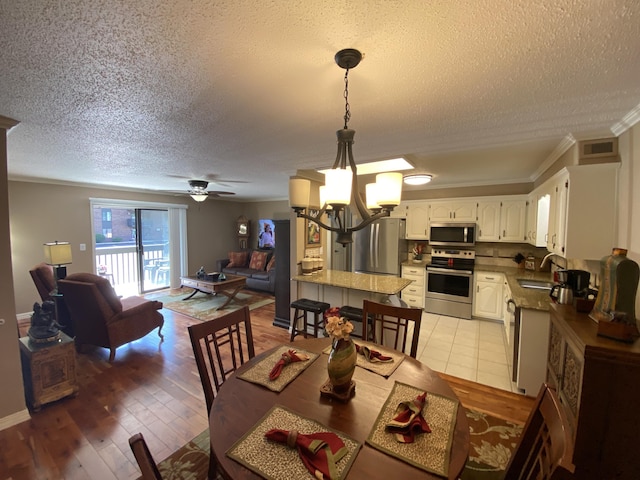 dining room with visible vents, ornamental molding, light wood-type flooring, a textured ceiling, and ceiling fan with notable chandelier